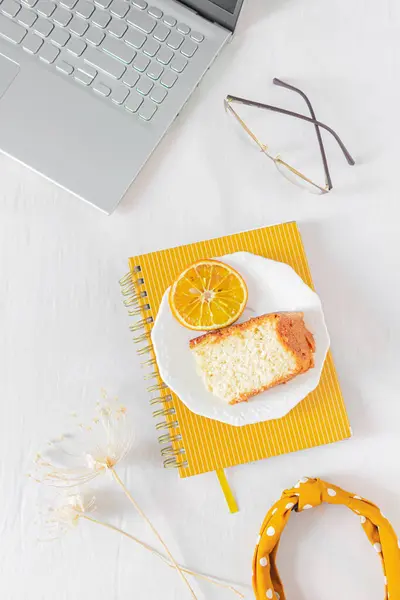 带有笔记本电脑 橙色蛋糕 米黄色野花和白色背景笔记本的家庭写字台框架 平躺在地上 尽收眼底 妇女的商业概念 — 图库照片