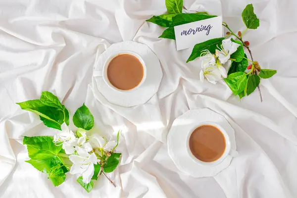牛奶和咖啡杯 卡片上有一句话 白花和黑莓叶落在凌乱的床上 春天的概念 可爱的夫妻早餐作文 — 图库照片