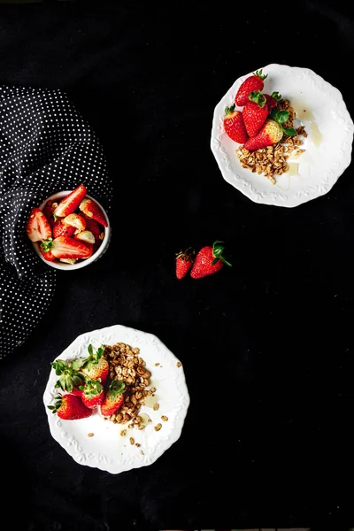 朝食のためのイチゴ 白いプレートと黒の背景にグラノーラと蜂蜜が付いているイチゴ — ストック写真