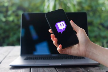 WROCLAW, POLAND - OCTOBER 2, 2023: Twitch logosu, arka planda MacBook Pro ile iPhone ekranında görüntülenen video oyunu canlı yayınına odaklanan bir Amerikan video canlı yayın servisidir.