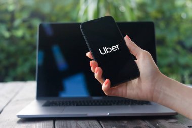 WROCLAW, POLAND - 2 Ekim 2023: Uber logosu, arka planda MacBook Pro ile iPhone ekranında gösterilen seyir hizmetleri, yemek teslimatı ve nakliye hizmeti veren şirket