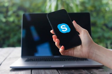 WROCLAW, POLAND - 2 Ekim 2023: Skype logosu, telekomünikasyon uygulaması, arka planda MacBook Pro ile iPhone ekranında görüntülendi