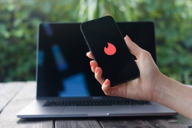WROCLAW, POLAND - 14 Eylül 2023: Tinder logosu, online flört uygulaması, arka planda MacBook Pro ile el ele tutulan iPhone 'da görüntülendi