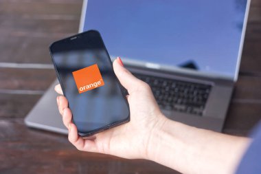 Orange logo, France Telecom markası - Fransız çokuluslu telekomünikasyon şirketi, arka planda MacBook Pro ile iPhone ekranında görüntülendi