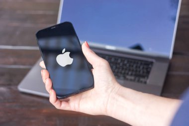 WROCLAW, POLAND - 14 Eylül 2023: Apple logosu, merkezi Cupertino, Kaliforniya 'da bulunan Amerikan bilişim şirketi, arka planda MacBook Pro ile iPhone ekranında sergilendi.