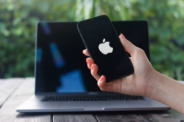 WROCLAW, POLAND - 14 Eylül 2023: Apple logosu, merkezi Cupertino, Kaliforniya 'da bulunan Amerikan bilişim şirketi, arka planda MacBook Pro ile iPhone ekranında sergilendi.