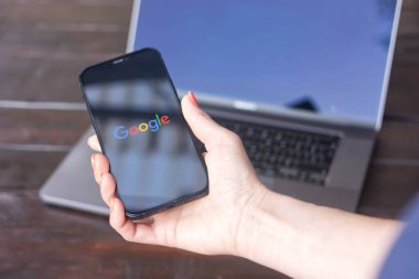 WROCLAW, POLAND - SEPTEMBER 14, 2023: Google logosu, Larry Page tarafından kurulan çok uluslu Amerikan teknoloji şirketi, arka planda MacBook Pro ile birlikte bir iPhone ekranında sergilendi.