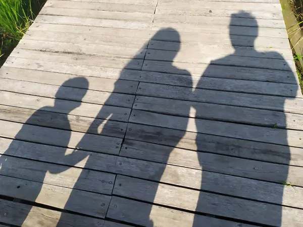 shadow of a small family photo between mother, father and son on a wooden background