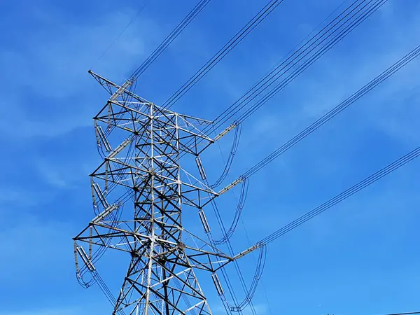 Mavi gökyüzü arka planında yüksek voltajlı elektrik iletim hatları kulesi.