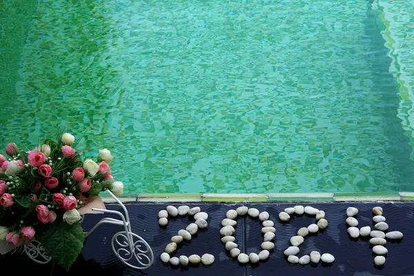 Ejderha Yılı ve Mutlu Yeni Yıl 2024 Taşlar tarafından zemin kaplamasında yazılan yapay güller yeşil yüzme havuzunu kapatıyor.
