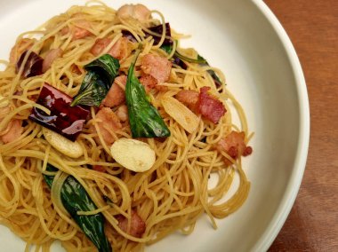 Kızarmış spagettiye yakın plan. Kurutulmuş biber ve ahşap arka planda kızarmış domuz pastırması..