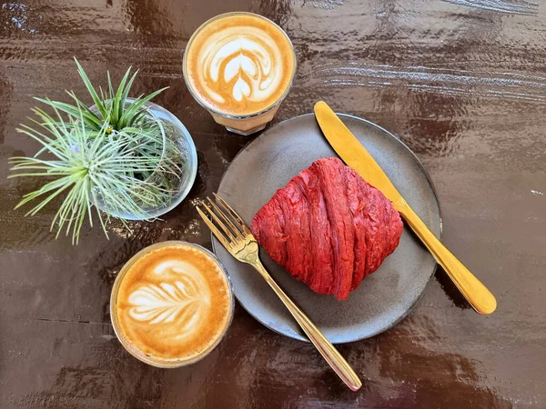 İki fincan sıcak latte sanat kahvesi ve kırmızı kadife kruvasan..