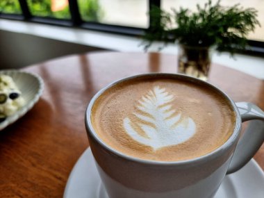 Tahta bir masada bir fincan sıcak latte sanat kahvesi..