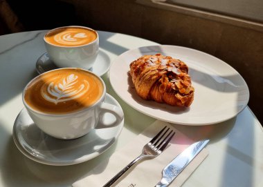 İki fincan sıcak latte sanat kahvesi ve kruvasan..