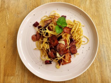 Kızarmış spagettiyi kurutulmuş biberle karıştırın ve ahşap arka planda beyaz tabakta kıtır pastırma..