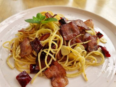 Yakın plan kızarmış spagetti, kurutulmuş biber ve ahşap arka planda beyaz bir tabakta kızarmış domuz pastırması..