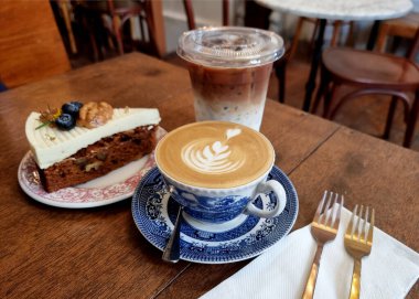 Bir fincan sıcak sütlü kahve ve masada kekli buzlu kahve..