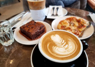 Bir fincan sıcak latte sanat kahvesi çikolatalı kek, pizza ve buzlu sütlü kahve.