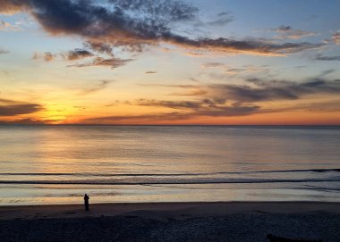 Gün doğmadan önce gökyüzünde güzel bulutlarla kumsalda yürüyen kadınlar.