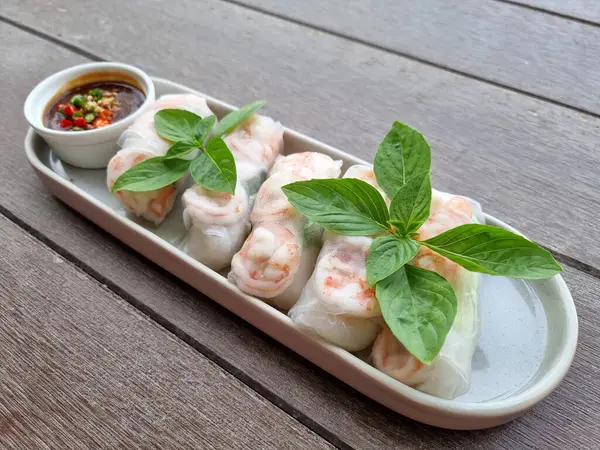 Fresh Vietnamese Spring Rolls with prawns and top-up basil leaves and sauces on wooden background