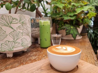 Tahta tabakta bir fincan sıcak sütlü kahve ve buzlu yeşil çay ve içme suyu..