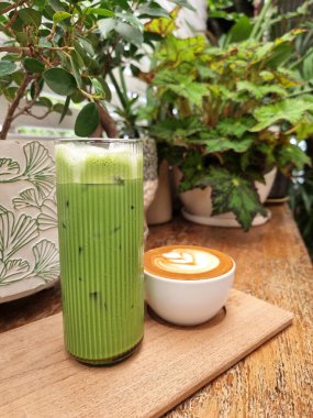 Bir fincan sıcak sütlü kahve ve ahşap tabakta buzlu yeşil çay.