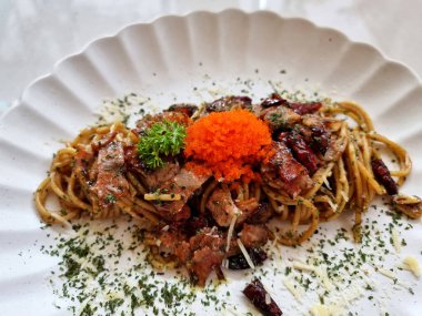 Yakın plan kızarmış spagetti, yanında kurutulmuş biber ve beyaz tabakta kızarmış domuz pastırması..