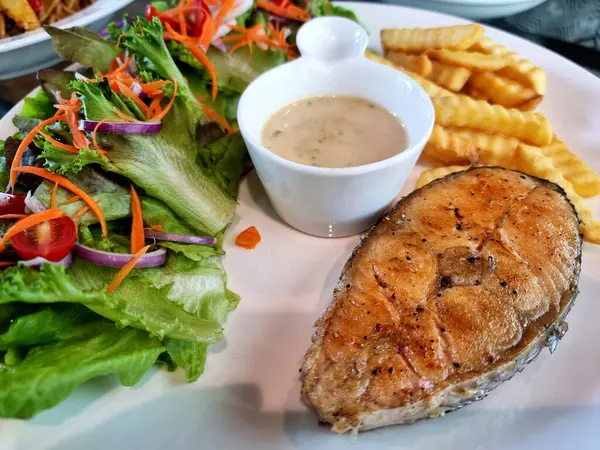 Tarhun soslu balık bifteği, salata ve patates kızartması. Beyaz tabakta..