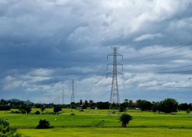 230 kV iletim hattı, taşrada bir pirinç tarlasında mavi gökyüzü arka planında bulutların üzerinde.