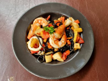 Tahta bir masada karides, kalamar ve sebze gibi deniz mahsullü spagetti siyah kalamar.