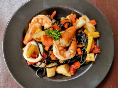Tahta bir masa üzerinde karides, kalamar ve sebze gibi deniz mahsulleri ile spagetti siyah kalamar yakın çekim