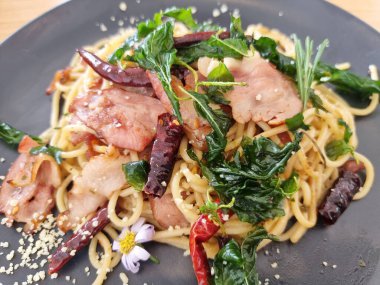 Yakın plan kızarmış spagetti ile kurutulmuş biber ve siyah tabakta kızarmış domuz pastırması..