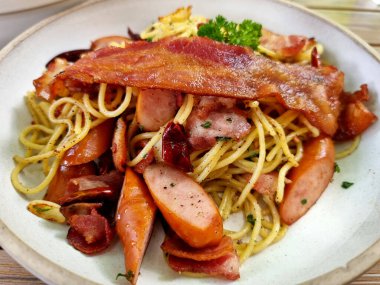 Baharatlı spagetti kuru biberli sarımsaklı pastırma ve beyaz tabakta sosis..