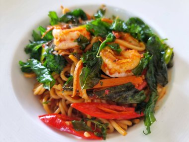 Karıştırılmış spagetti makarna, karides ve kutsal fesleğen yaprakları beyaz tabakta.