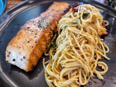 Somon bifteği ve siyah tabakta kurutulmuş acı biberli kızarmış spagetti.