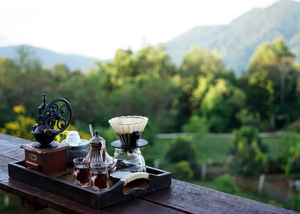 Kahve damlatıcısının seti ahşap bir masa ve bulanık yeşil bir bahçe arka planında Manual Coffee Grinder, Pour Over Kettle, Coffee Dripper, 2 Tadım Kâğıdı, Kahve Filtresi
