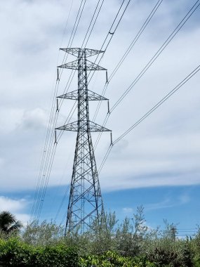 Elektrik Aktarım Hattı 'nın dikey görüntüsü Yüksek Voltaj Kulesi bulutların üzerinden geçiyor ve mavi gökyüzü arkaplanı.