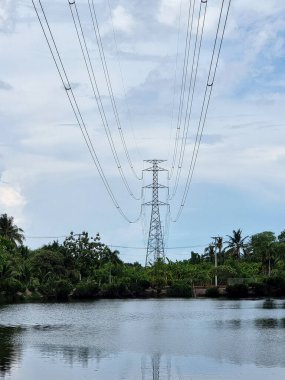 Elektrik Aktarım Hattı 'nın dikey görüntüsü. Yüksek voltajlı kule bulutlar ve mavi gökyüzü arka planında bir göletin üzerinden geçiyor..