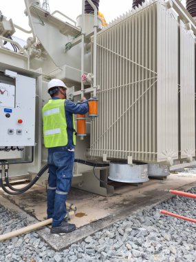 Vertical shot of Orange Silica Gel replacement activity by electrician for Silica Gel Breather at main tank and OLTC of 115kV/22kV power transformer., Transformer preventive maintenance. clipart