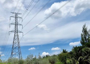 Elektrik iletim hattı yüksek voltajlı kule bulutların üzerinden geçiyor ve mavi gökyüzü arkaplanı.