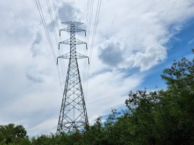 Elektrik iletim hattı yüksek voltajlı kule bulutların üzerinden geçiyor ve mavi gökyüzü arkaplanı.