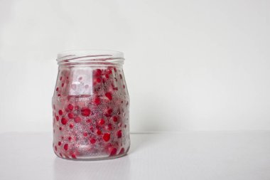 Cam bir kavanozda kırmızı frenk üzümü, kapağı olmayan beyaz bir yüzey ve mutfakta beyaz bir zemin üzerinde duruyor.