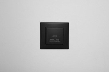 Beyaz bir duvarda siyah USB şarj aleti. Telefon, tablet, el feneri, saat, elektrik bankaları ve diğer elektronik cihazlar gibi cihazları şarj etmek için iki girdiyle kare biçiminde.
