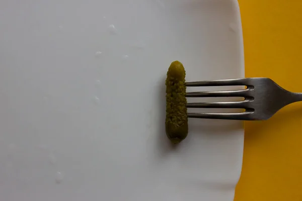 Yeşil ve küçük salatalık turşusu beyaz tabakta çelik çatal ve mutfakta sarı masa. Ev yapımı yiyecekler, koruma, sebzeler, sosyal yardımlar, sağlık. Kafeler, restoranlar, yemek şirketleri, şef