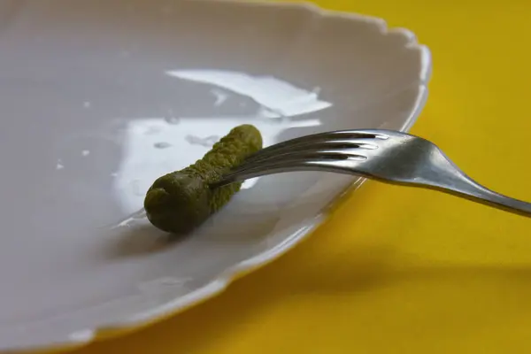 Yeşil ve küçük salatalık turşusu beyaz tabakta çelik çatal ve mutfakta sarı masa. Ev yapımı yiyecekler, koruma, sebzeler, sosyal yardımlar, sağlık. Kafeler, restoranlar, yemek şirketleri, şef
