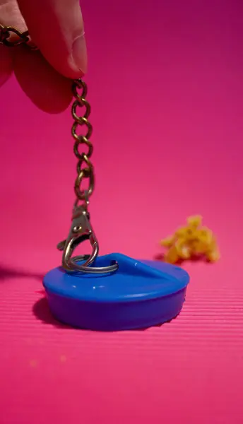 Mavi banyo tıkacı. Lastikten yapılmış. Elinde zincirle. Parlak pembe arka plan. Banyo, hijyen, ev aletleri. Tesisat
