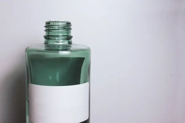 Yeşil cam kavanoz, üzerinde sıvı parfüm, beyaz, temiz etiket, ahşap tezgahın üzerinde bambu sopaları var. İlaç, güzellik ve bakım, kozmetik ürünler, kokular. Yazı için yer. Sanayi, üretim