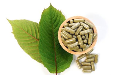 Taze yeşil Kratom yaprakları ve beyaz arka planda izole edilmiş bitki tozu kapsülleri.