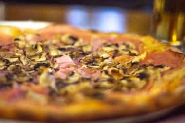 Restorandaki ahşap bir masada jambonlu ve mantarlı pizza.,