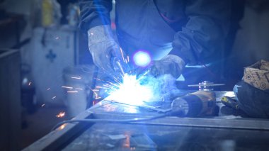 İşçi, kaynakçı, iş kıyafetleri, inşaat eldivenleri ve bir kaynak maskesiyle kaynak makinesi, Kocani Makedonya yakınlarındaki atölye çalışmasında kullanılıyor.